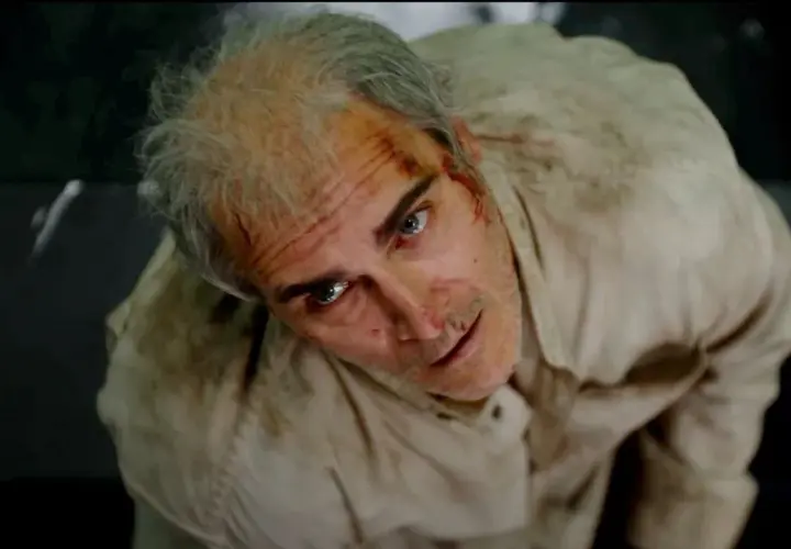 Un uomo con i capelli grigi e ferite sul viso, vestito di una camicia sporca, guarda in alto con espressione spaventata. Beau ha paura, spiegazione visiva.