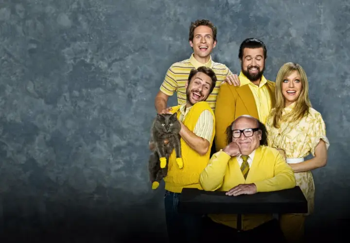 Il cast di "C'è sempre il sole a Philadelphia" posa sorridendo, con Charlie che tiene un gatto grigio con calzini gialli.