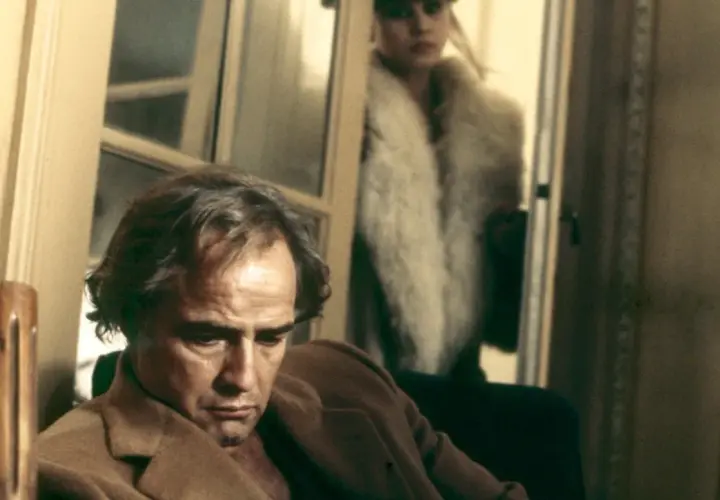 Marlon Brando pensieroso, sullo sfondo Maria Schneider in pelliccia. Scena iconica di "Ultimo tango a Parigi", la scena del burro.