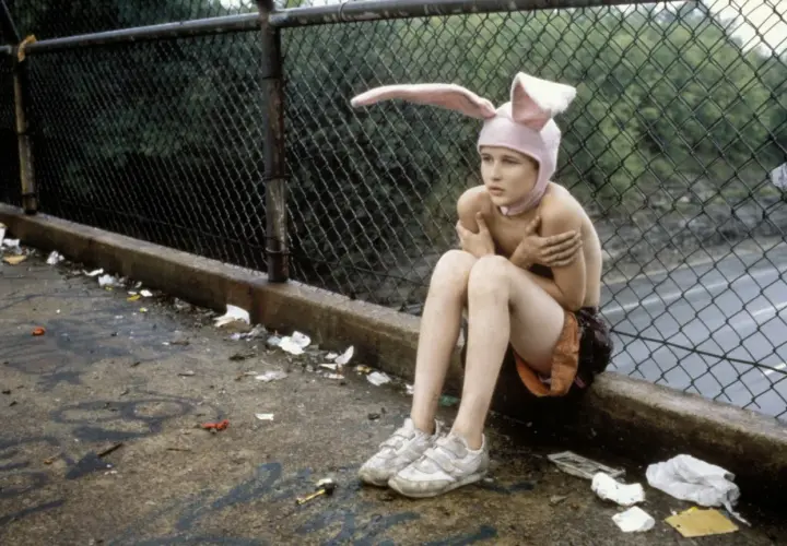 Bambino con cappello da coniglio seduto su un marciapiede sporco, un'immagine che evoca la trama di Gummo.