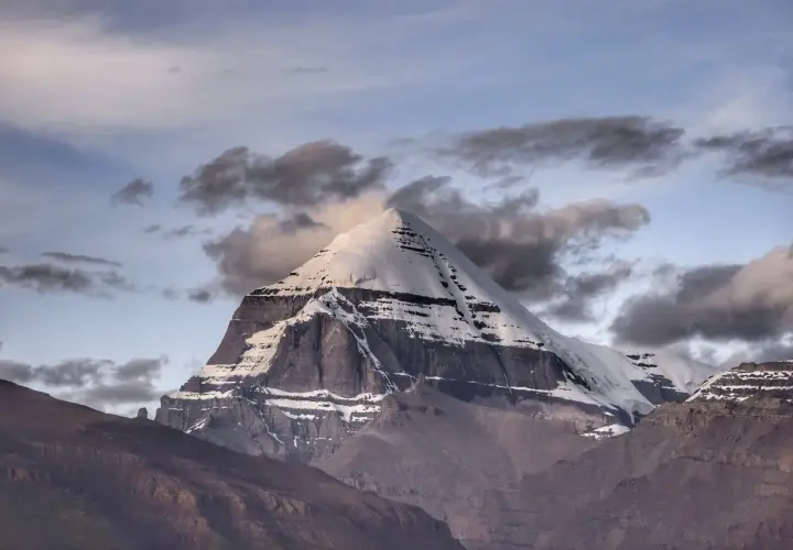 La montagna sacra spiegazione: il maestoso Kailash, coperto di neve, si erge tra nuvole scure e un cielo crepuscolare, simbolo di spiritualità e mistero.