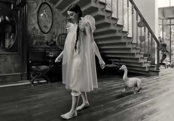 Bella Baxter, con un'aria sognante, cammina a piedi nudi in una casa d'epoca, accompagnata da un'oca e un cane.
