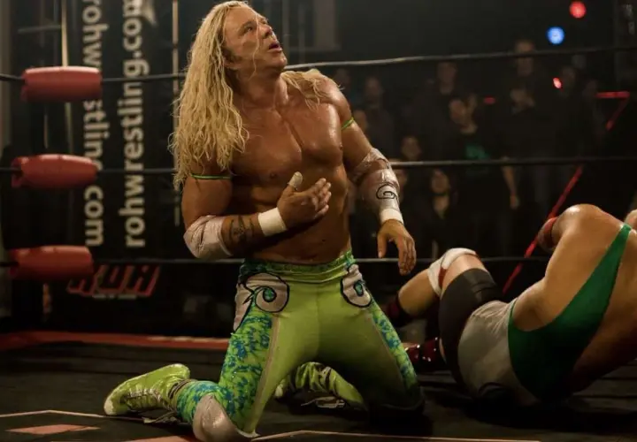 Randy the Ram, il wrestler dai lunghi capelli biondi, in ginocchio sul ring, guarda verso l'alto con espressione intensa.