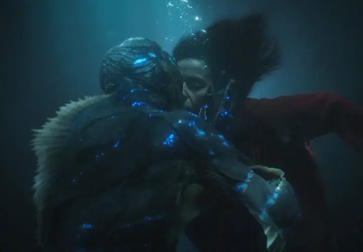 La forma dell'acqua recensione: un bacio subacqueo tra una donna e una creatura anfibia, illuminati da luci blu bioluminescenti.