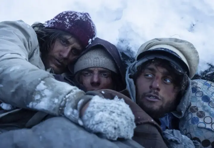 Tre uomini stremati nel gelo, un'immagine che evoca le recensioni de "La società della neve", la lotta per la sopravvivenza.