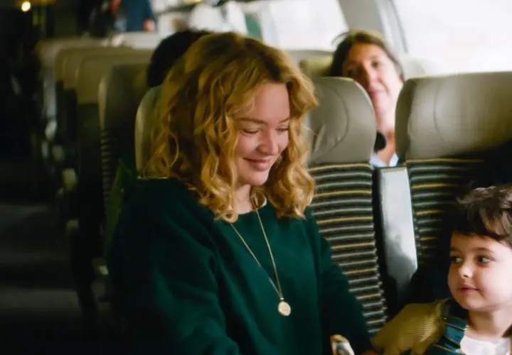 Una donna sorride mentre guarda un bambino su un treno. Le recensioni de "I figli degli altri" lodano questa scena.
