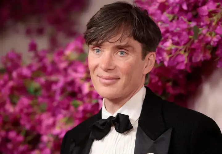 Cillian Murphy, l'attore di Oppenheimer, con un sorriso enigmatico e occhi azzurri penetranti, indossa un elegante smoking con papillon nero.