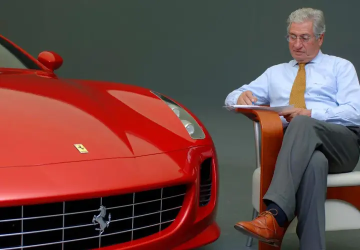 Un uomo d'affari con una cravatta gialla scrive appunti accanto a una Ferrari rossa, forse per le recensioni del film.