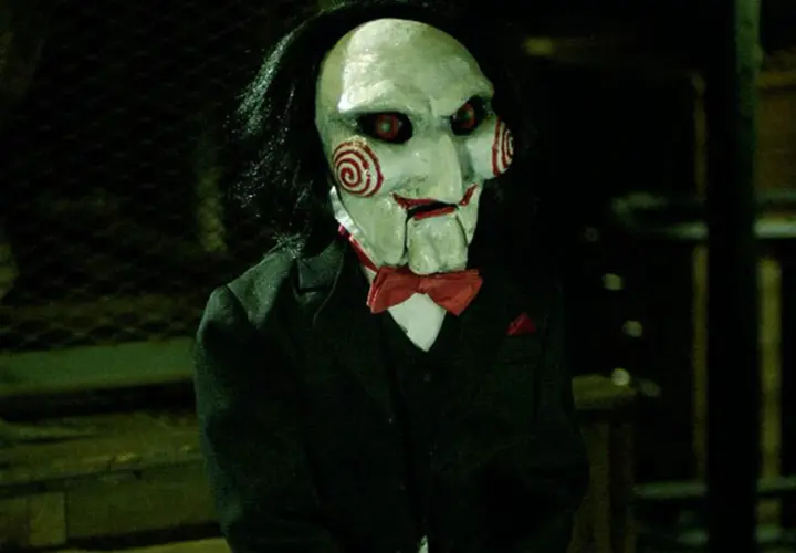 La maschera di Billy, il pupazzo di **jigsaw saw**, con i suoi vortici rossi e occhi rossi, indossa un abito elegante.