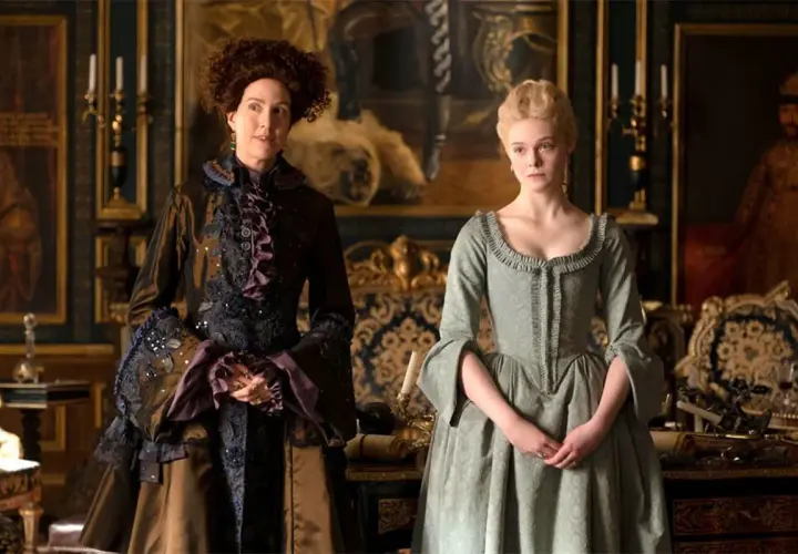 Due donne in abiti storici, una con capelli ricci e un vestito scuro elaborato, l'altra con capelli biondi raccolti e un abito verde chiaro. Le loro espressioni suggeriscono un momento di tensione, forse in attesa di grandi recensioni.