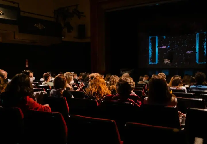 Pubblico in sala, immerso nell'oscurità, attende con il fiato sospeso i monologhi da brividi che stanno per iniziare sul palco illuminato.