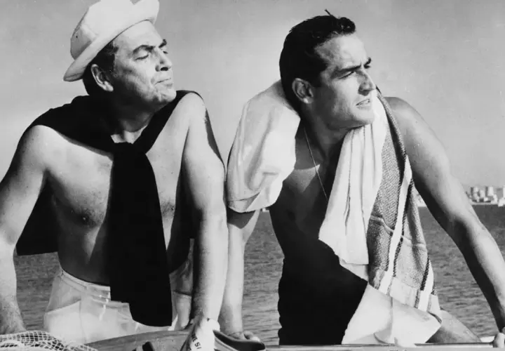Due uomini su una barca, uno con un berretto da marinaio e una sciarpa, l'altro con un asciugamano. Un'immagine che evoca il significato del sorpasso, film e vita.