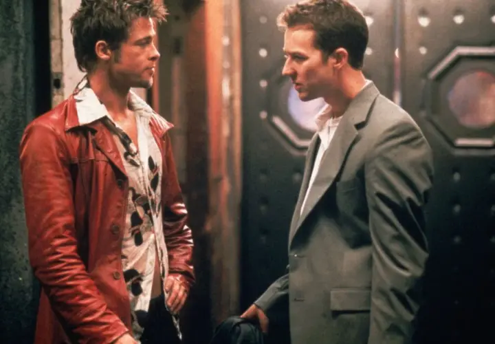 Il narratore di Fight Club, con la sua giacca rossa, parla con un uomo in completo grigio.