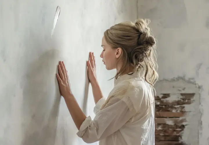 Una madre in un film, con le mani sul muro, sembra cercare una spiegazione o un conforto.