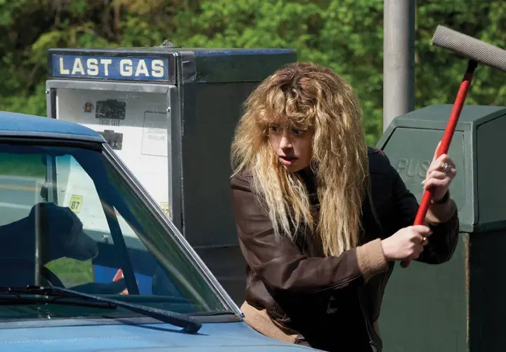 La protagonista di Poker Face, Nadia Vulvokov, con i suoi capelli biondi spettinati, impugna un tergivetro rosso davanti a una pompa di benzina "Last Gas".