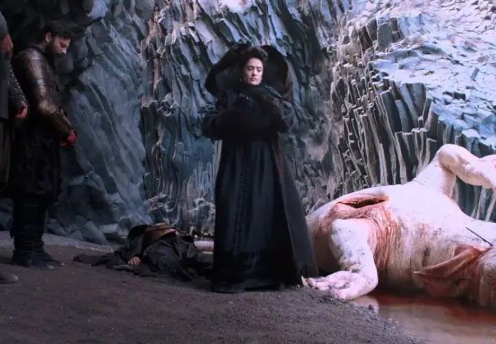 Una donna in nero osserva un mostro acquatico morto, con guerrieri al fianco. Scena da "Il racconto dei racconti recensione".