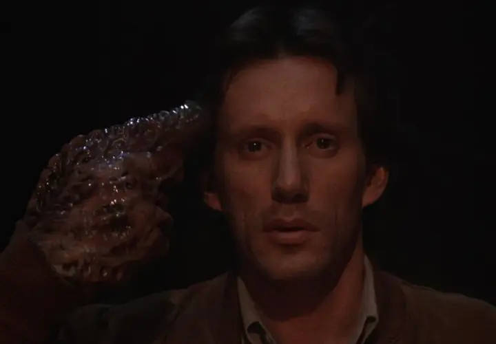 Un uomo con una mano mutata, simile a un tumore, punta alla tempia. Un'immagine disturbante che riflette il videodrome significato.