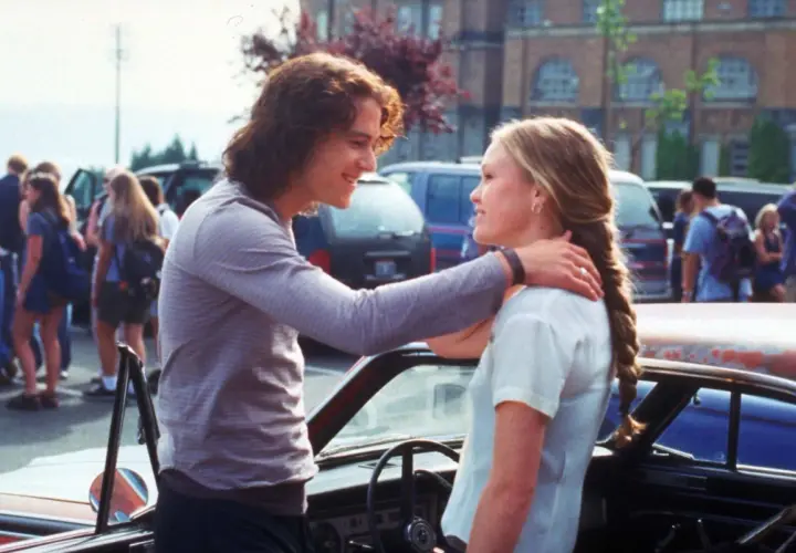 Il cast di "10 cose che odio di te" con Heath Ledger e Julia Stiles che si guardano sorridendo vicino a un'auto.