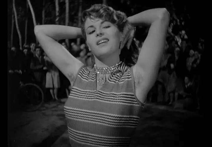 Una donna con le braccia alzate, un sorriso sulle labbra e un'espressione che evoca il "riso amaro significato". Sullo sfondo, una folla indistinta.