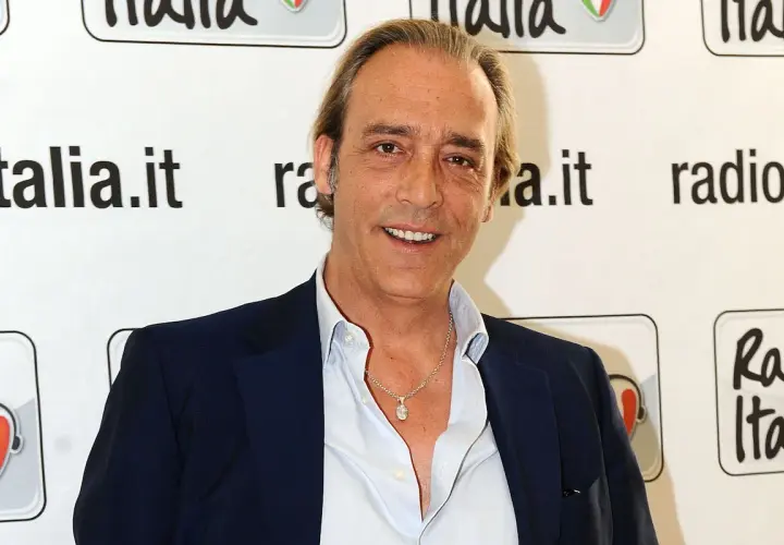 Luca Ward, noto per i suoi ruoli in film e programmi TV, sorride davanti a uno sfondo con il logo di Radio Italia.