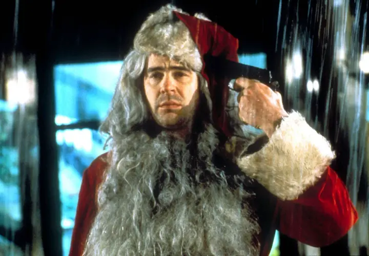 Un uomo con barba e cappello da Babbo Natale tiene una pistola puntata alla tempia. Sembra una scena da "Una poltrona per due Babbo Natale".