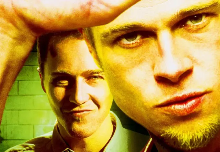 Primo piano di due uomini, uno con uno sguardo intenso, l'altro sorride. L'immagine evoca il **fight club significato** di ribellione e ricerca di identità.
