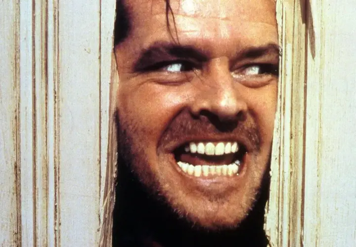 Occhi bianchi e un sorriso folle, un volto che spunta da una porta in un momento di terrore shining congelato.