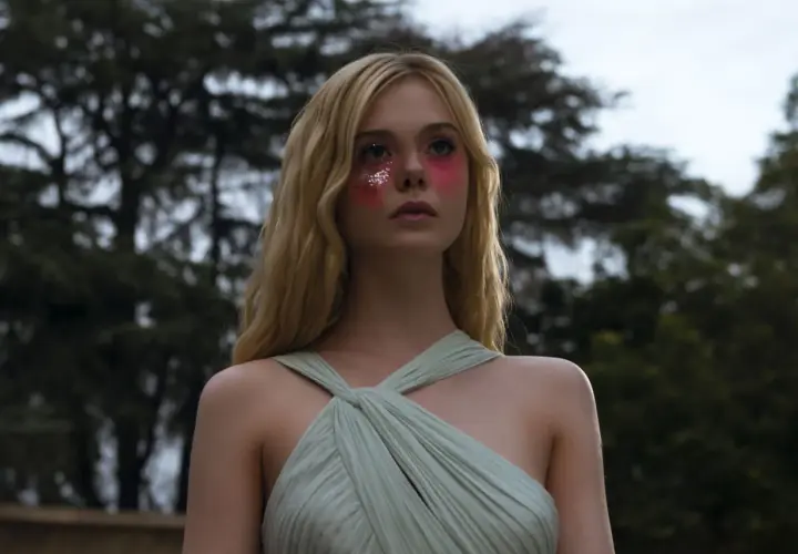 Ragazza con trucco glitterato e vestito verde pallido, un'immagine che evoca il significato di "The Neon Demon" e la sua ossessione per la bellezza.