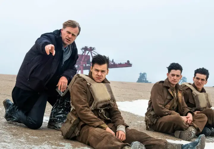 Il cast di Dunkirk, con Christopher Nolan che dirige i giovani soldati seduti sulla spiaggia.