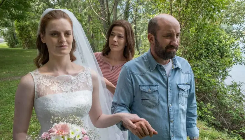 Sposa con velo e bouquet, accompagnata da un uomo in camicia di jeans e una donna sullo sfondo. Scena del **cento domeniche finale**.