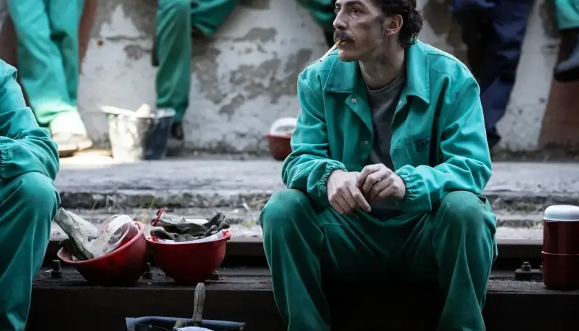 Uomo con baffi, in tuta verde, fuma una sigaretta. Le sue mani sono giunte, sembra pensieroso. Le recensioni per la palazzina LAF potrebbero essere simili.