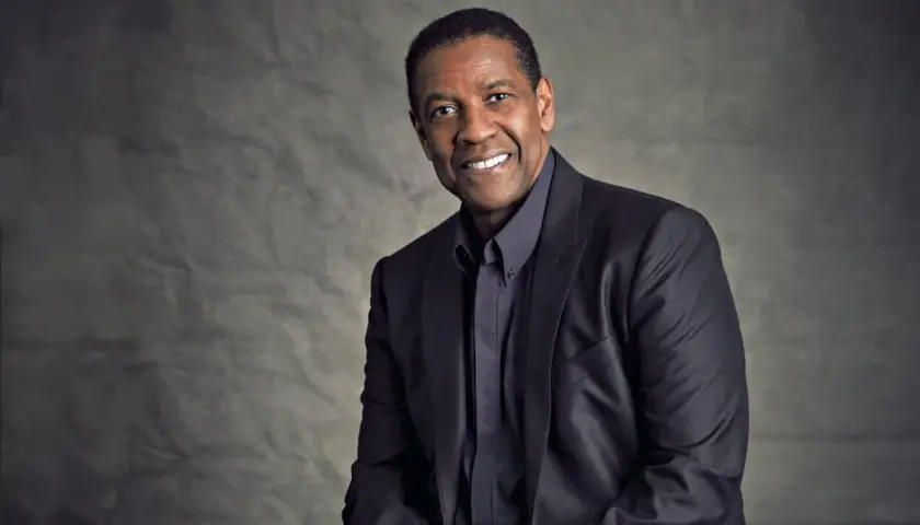 Ritratto di Denzel Washington, attore e doppiatore, con un sorriso caloroso e un abito scuro.