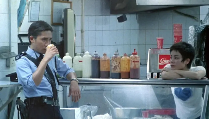 Un poliziotto sorseggia una bevanda, mentre una ragazza appoggia il mento sulle mani. Scena da "Hong Kong Express" con spiegazione implicita.