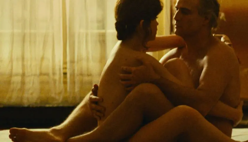 Una scena intima di sesso al cinema, con una coppia abbracciata in un letto, illuminata da una luce soffusa.