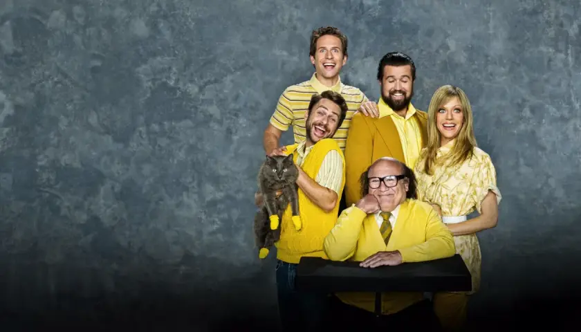 Il cast di "C'è sempre il sole a Philadelphia" posa sorridendo, con Charlie che tiene un gatto grigio con calzini gialli.