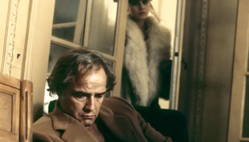Marlon Brando pensieroso, sullo sfondo Maria Schneider in pelliccia. Scena iconica di "Ultimo tango a Parigi", la scena del burro.
