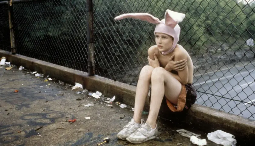 Bambino con cappello da coniglio seduto su un marciapiede sporco, un'immagine che evoca la trama di Gummo.