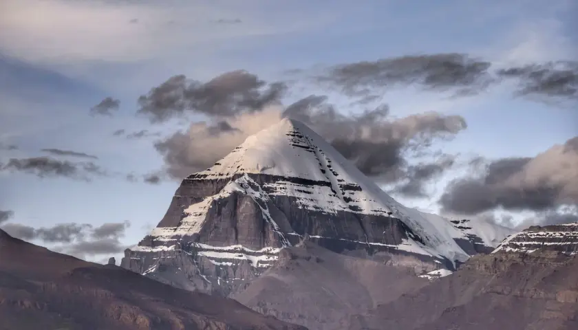 La montagna sacra spiegazione: il maestoso Kailash, coperto di neve, si erge tra nuvole scure e un cielo crepuscolare, simbolo di spiritualità e mistero.