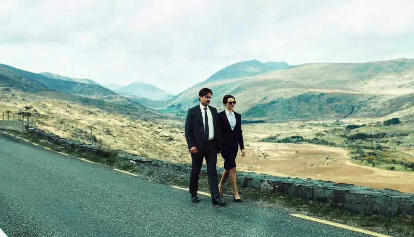 Coppia in abito cammina su strada panoramica, paesaggio montuoso. Un'immagine che evoca la recensione di "The Lobster".