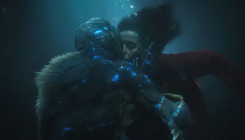 La forma dell'acqua recensione: un bacio subacqueo tra una donna e una creatura anfibia, illuminati da luci blu bioluminescenti.