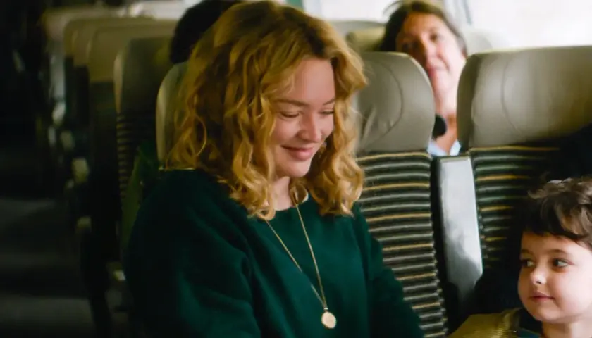 Una donna sorride mentre guarda un bambino su un treno. Le recensioni de "I figli degli altri" lodano questa scena.