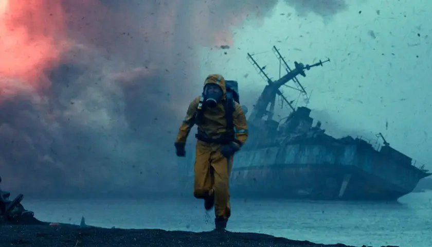 Uomo in tuta gialla corre su una spiaggia desolata, con una nave naufragata sullo sfondo. Le recensioni di Greenland descrivono scene apocalittiche simili.
