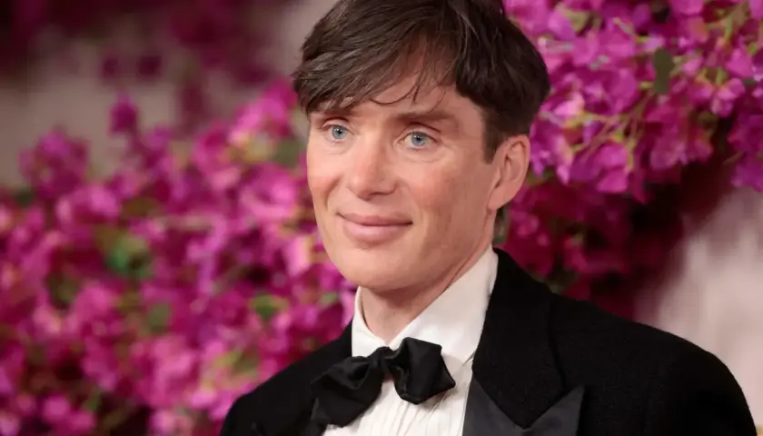 Cillian Murphy, l'attore di Oppenheimer, con un sorriso enigmatico e occhi azzurri penetranti, indossa un elegante smoking con papillon nero.