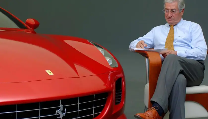 Un uomo d'affari con una cravatta gialla scrive appunti accanto a una Ferrari rossa, forse per le recensioni del film.