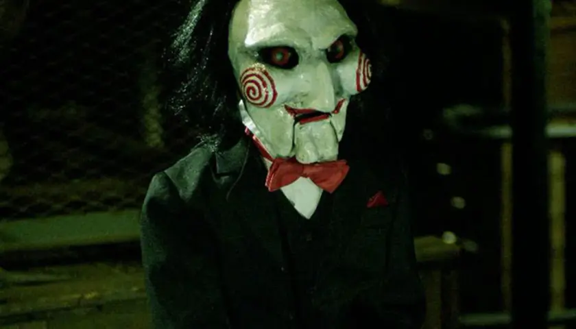 La maschera di Billy, il pupazzo di **jigsaw saw**, con i suoi vortici rossi e occhi rossi, indossa un abito elegante.