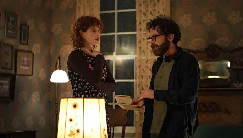 Una donna con capelli rossi e un uomo con occhiali discutono animatamente in una stanza. Lui tiene un quaderno, forse sto pensando di finirla qui recensioni.