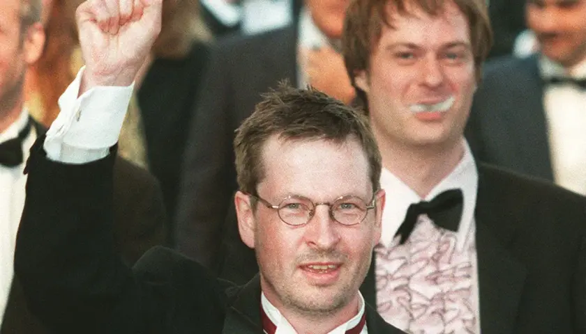 Lars von Trier, regista, alza il pugno in segno di vittoria, circondato da festeggiamenti.