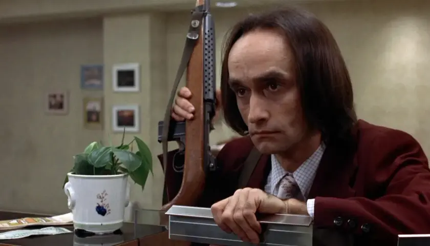 Un uomo con un fucile a tracolla, forse in una scena che ricorda il john cazale funeral, guarda intensamente.