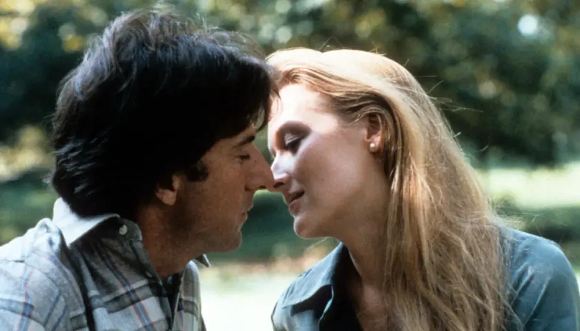 Un tenero momento tra John Cazale e Meryl Streep, i loro volti vicini in un abbraccio intimo.