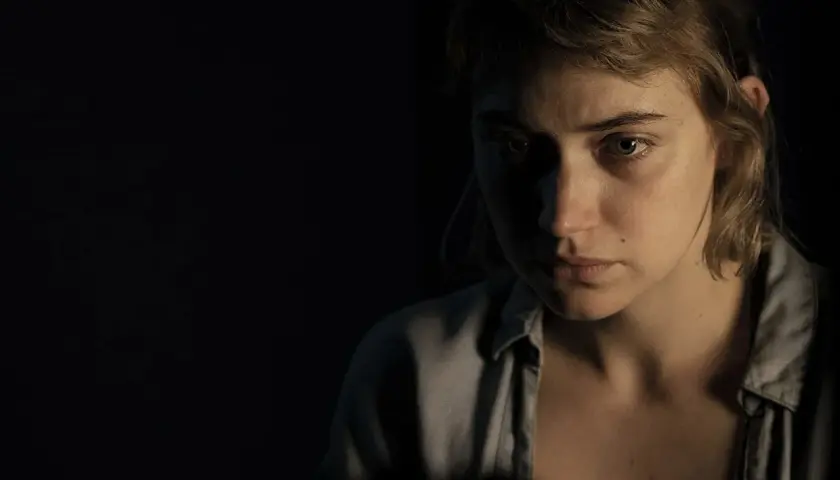 Primo piano di una giovane donna con sguardo preoccupato, in penombra. Un'immagine che evoca le atmosfere di "Vivarium", recensione.